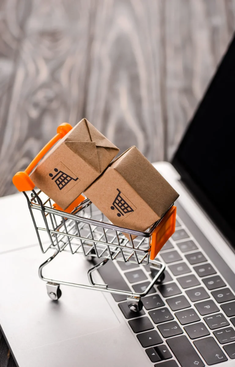 selective focus of toy carton boxes in small shopping cart on laptop with blank screen, e-commerce